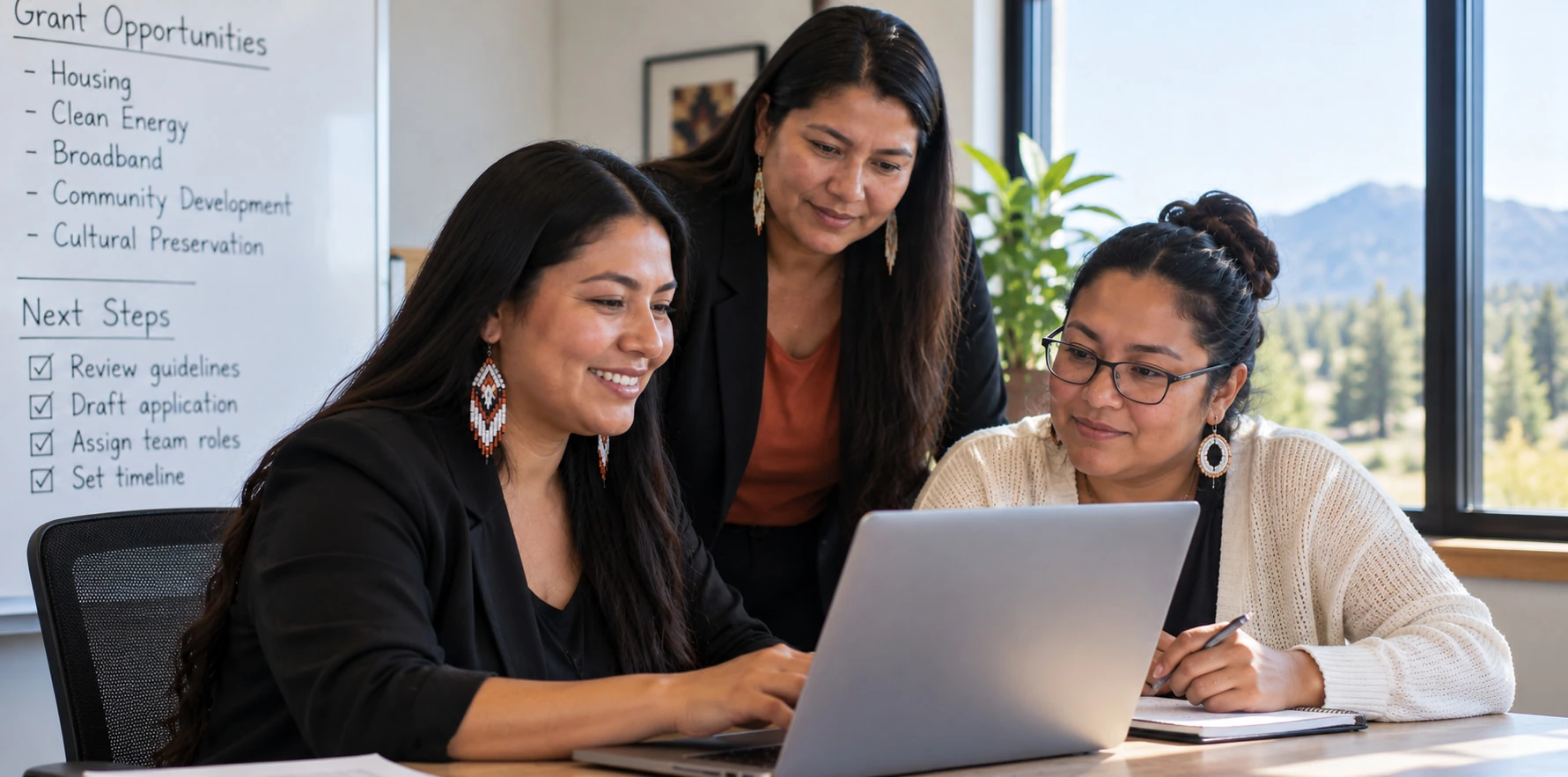 Three members of a Tribal grants team smiling over a laptop, with a whiteboard of grant opportunities and next steps behind them
